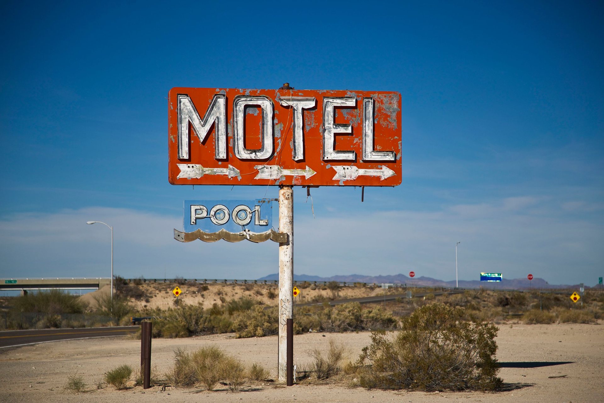 Weathered orange roadside motel sign with two arrows and a pool sign beside a highway