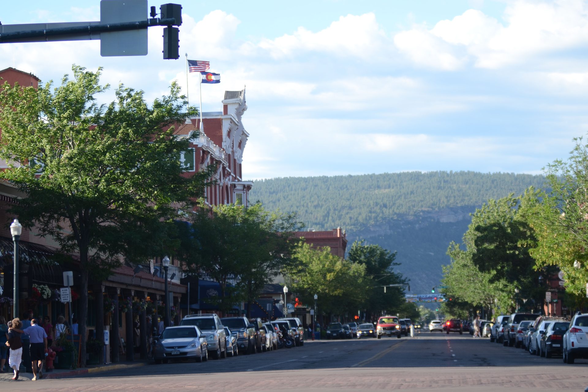 Tree-lined Main Avenue in downtown Durango, with parked cars along the curb and wooded hills at the end of the street