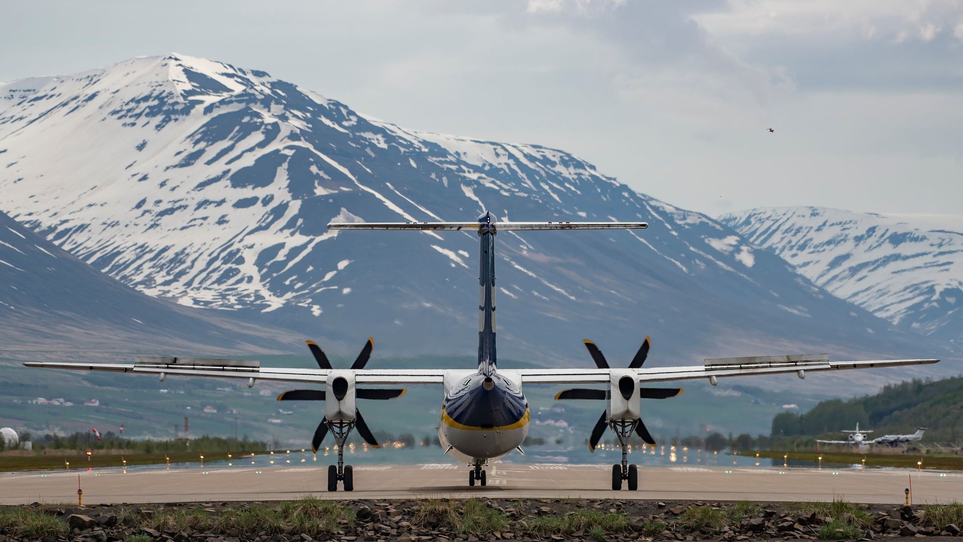 Twin-engine turboprop airliner facing the camera on an airport runway with snow-capped mountains rising behind