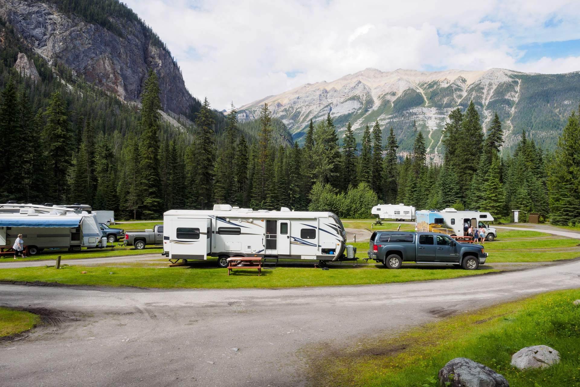 Travel trailers and a pickup parked on a campground loop below forested mountains