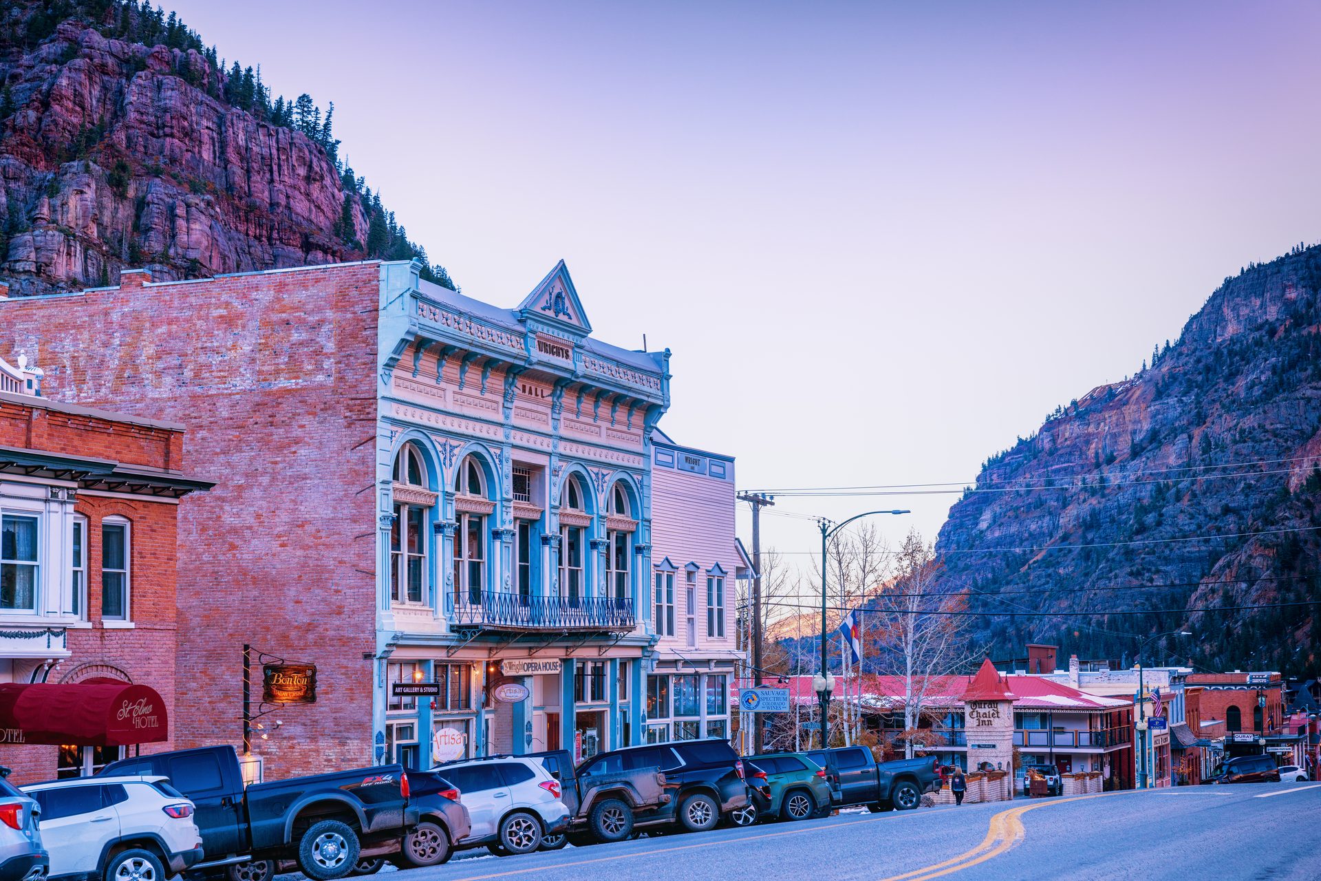 Historic brick storefronts on Main Street in Ouray at sunset, with red cliffs rising behind the town