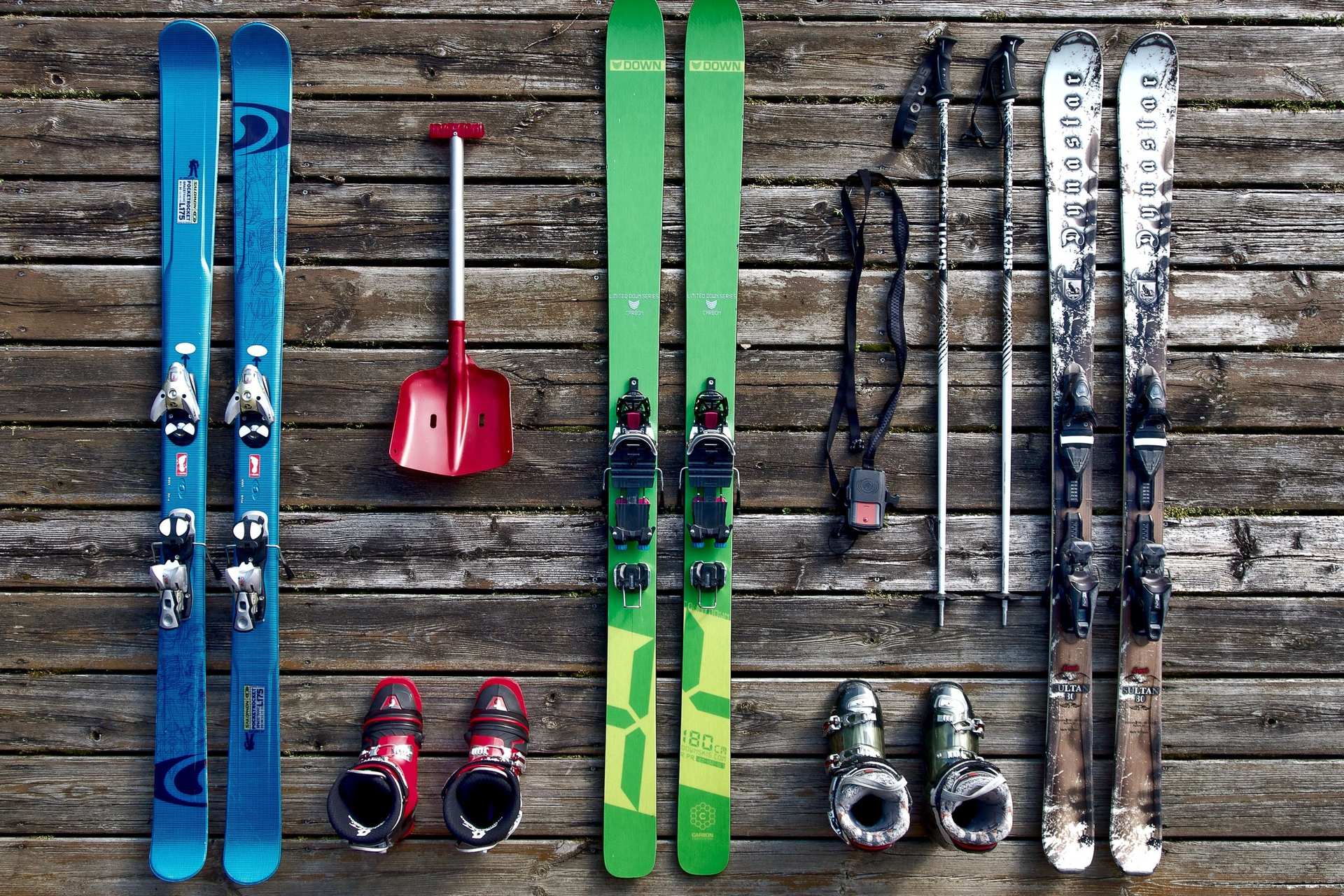 Skis, ski boots, poles and an avalanche shovel laid out in rows on a wooden deck