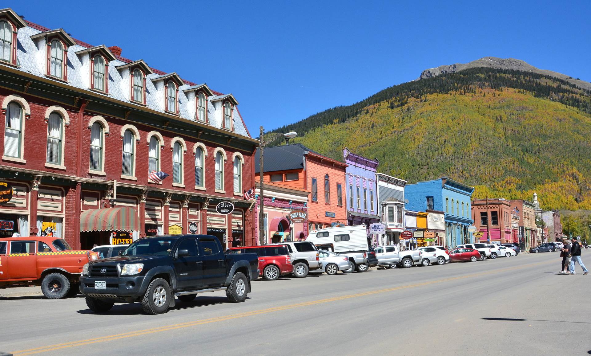 Victorian brick and painted storefronts along Silverton's main street, with a hillside of aspen color above town