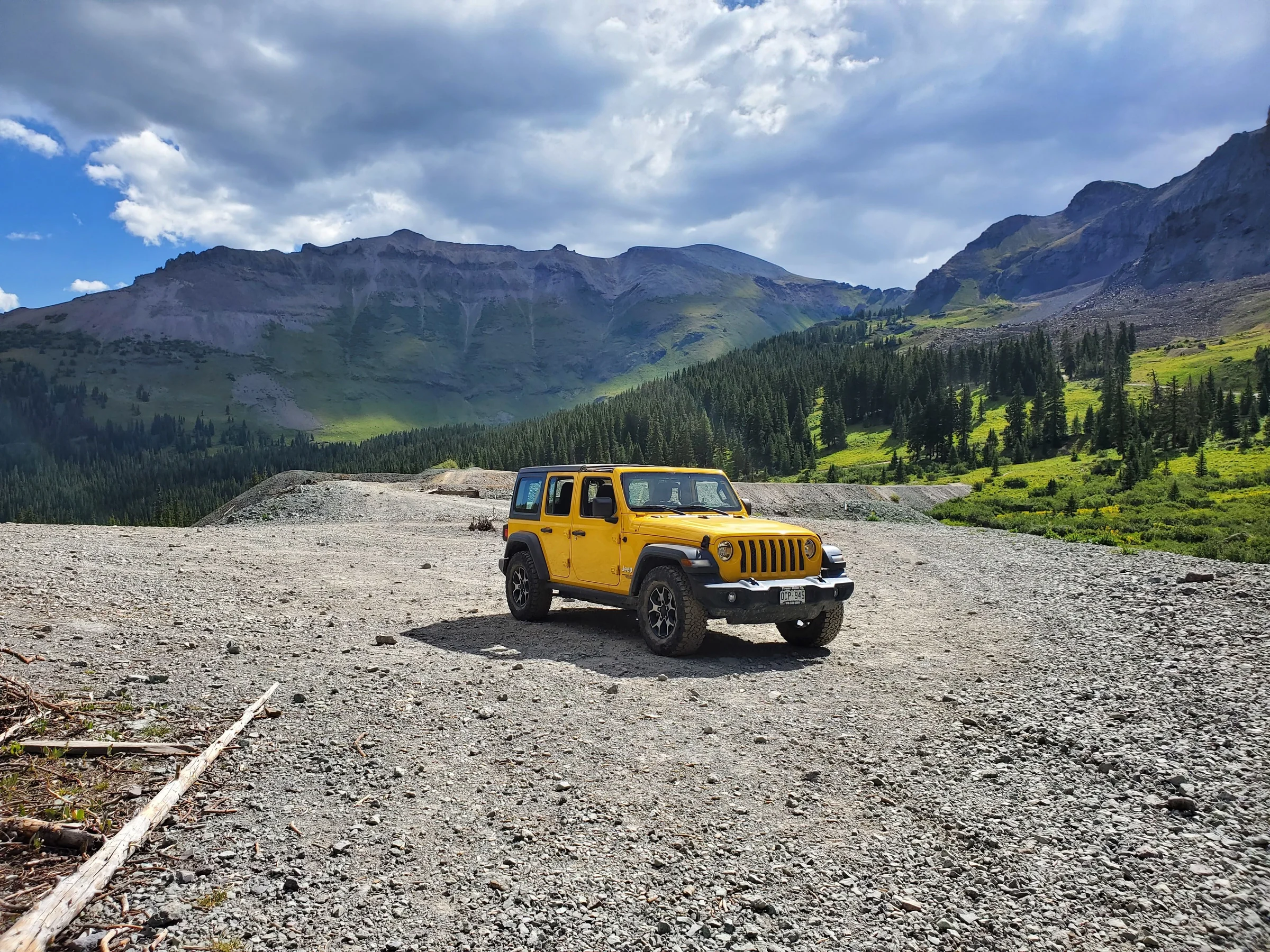A yellow Jeep Wrangler parked on a gravel road in a high mountain valley